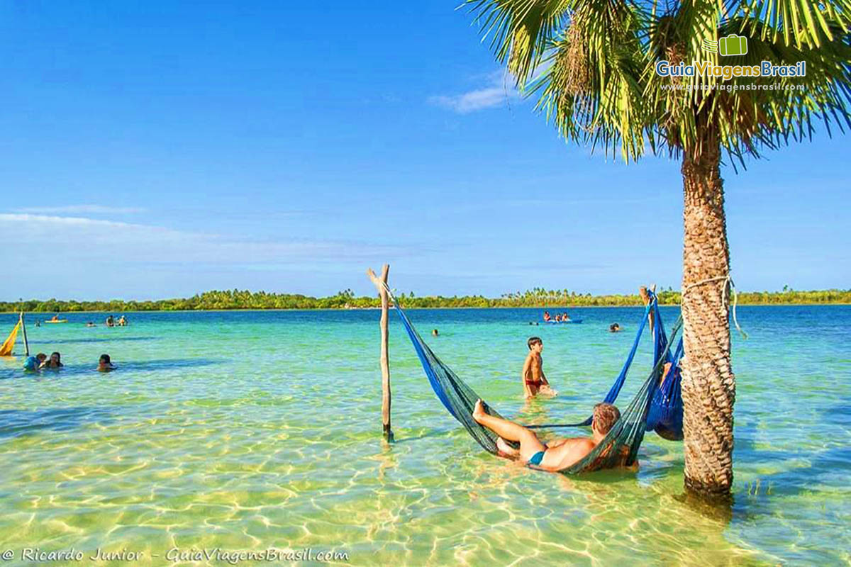 Imagem de turistas deitado na rede dentro das lagoa aproveitando o belo dia de sol.