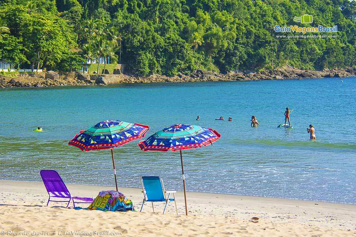 Imagem de dois guarda sol na praia e pessoas nas águas da Praia Barra do Sahy.