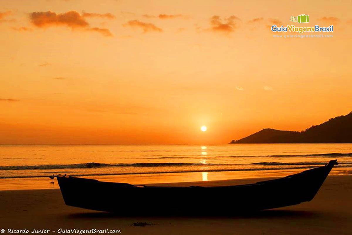 Imagem de um barco de pescador na areia e ao fundo lindíssimo entardecer.