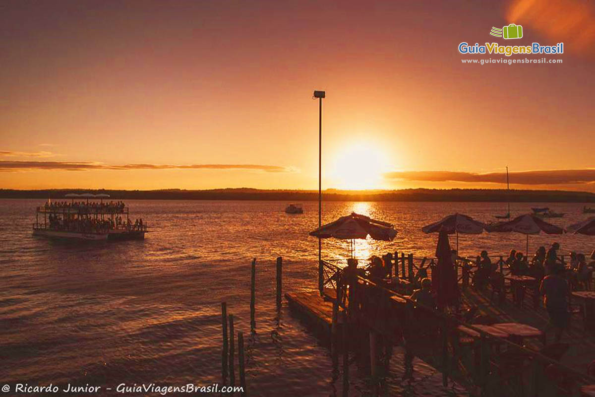 Imagem de turistas no deck e no barco de passeio admirando o fantástico pôr do sol na praia.