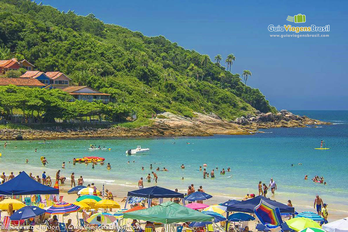 Imagem de guarda sol nas areias da praia e no mar pessoa praticando esportes.