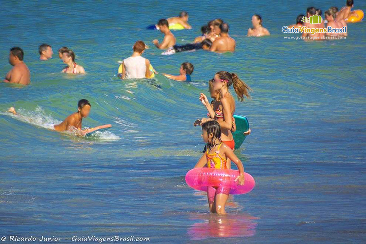 Imagem de crianças entrando com bóia nas águas do mar.