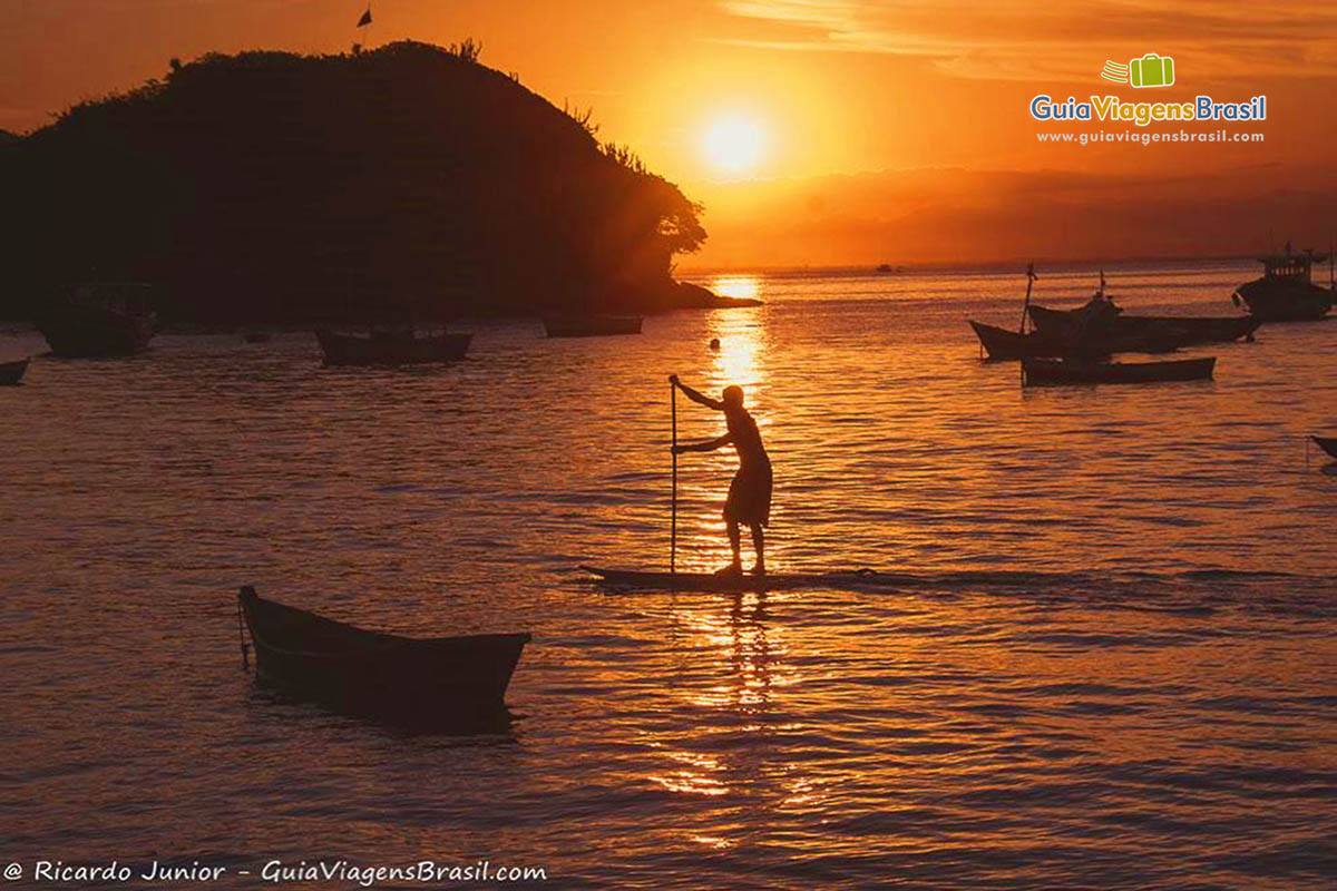 Imagem do um pescador no mar e o sol se pondo no mar.