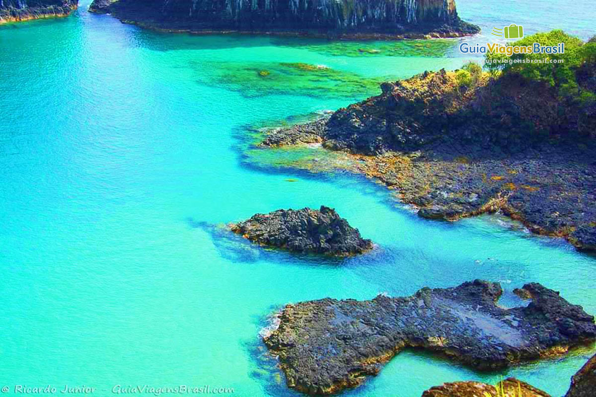 Imagem das águas da Baía dos Porcos, águas muito claras que é possível ver o fundo, conseguimos enxergar a areia e as pedras, em Fernando de Noronha, Pernambuco, Brasil.