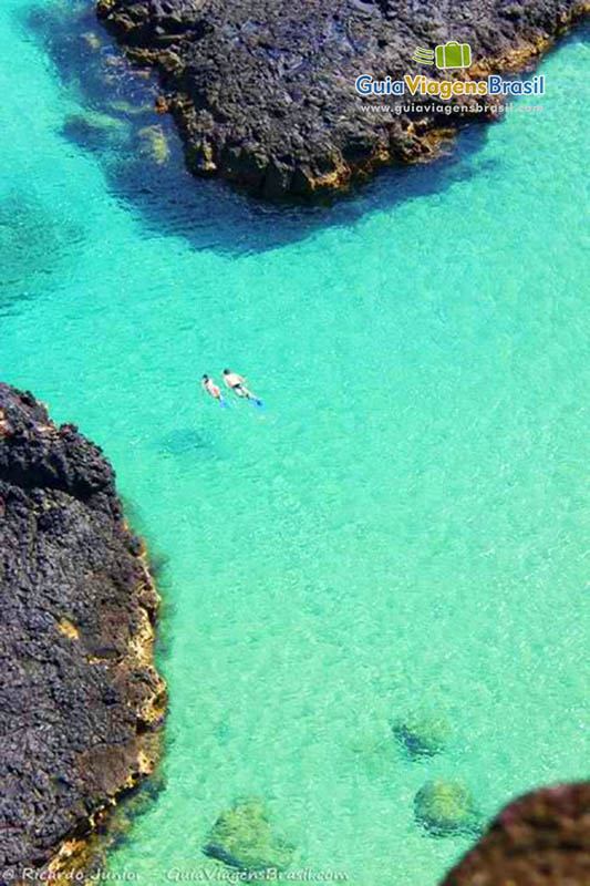 Imagem do alto e lá embaixo nas águas translúcidas turistas mergulhando, na Baía dos Porcos, em Fernando de Noronha, Pernambuco, Brasil. 