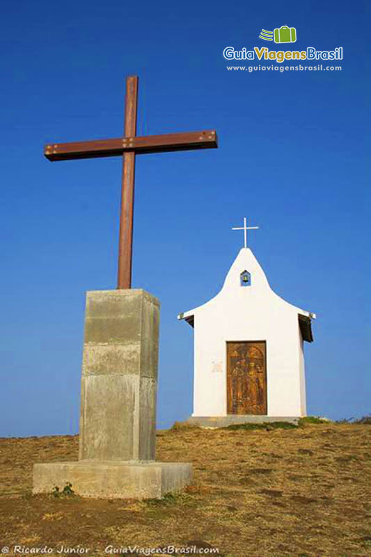 Imagem da Capela de São Pedro e um pouco a frente um crucifixo  grande de madeira, em Fernando de Noronha, Pernambuco, Brasil.
