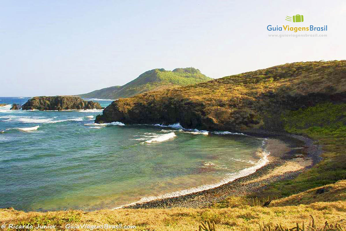 Imagem de toda extensão da Enseada dos Tubarões e no alto a Capela de São Pedro, em Fernando de Noronha, Pernambuco, Brasil.