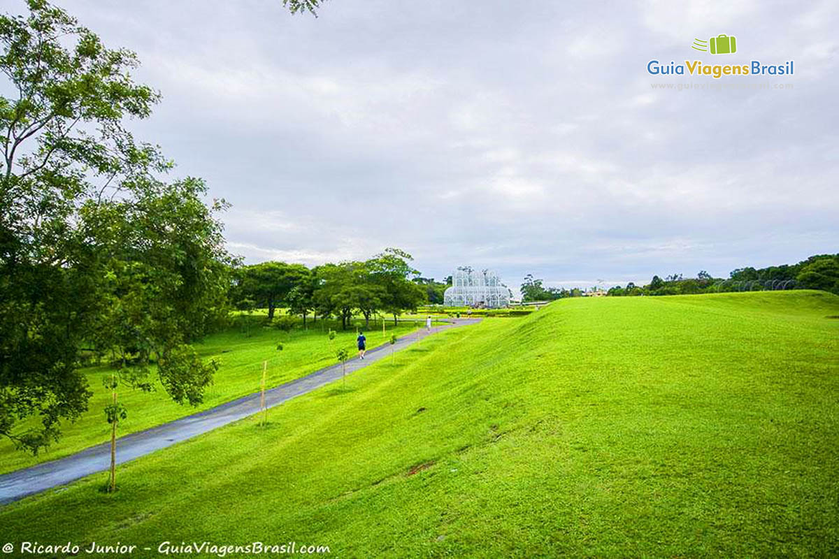 Imagem da grande área de gramado no Jardim Botânico e ao fundo a bela estufa.