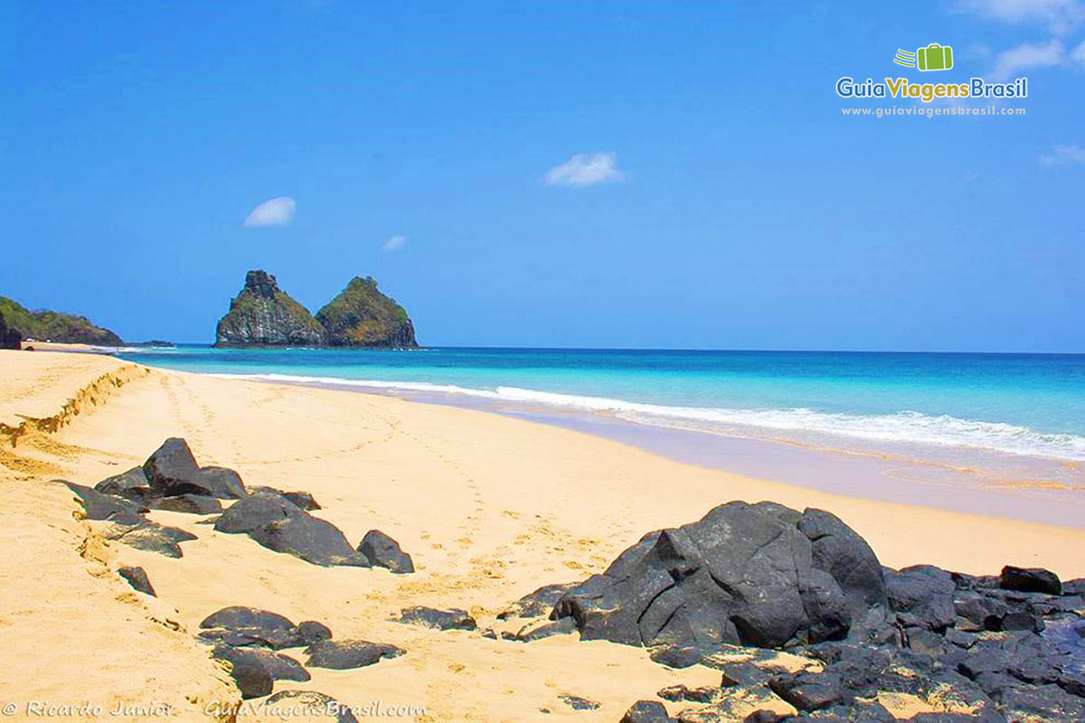 Imagem de rochas na areia da praia, fazendo bela composição com o Morro Dois Irmãos ao fundo, em Fernando de Noronha, Pernambuco, Brasil.