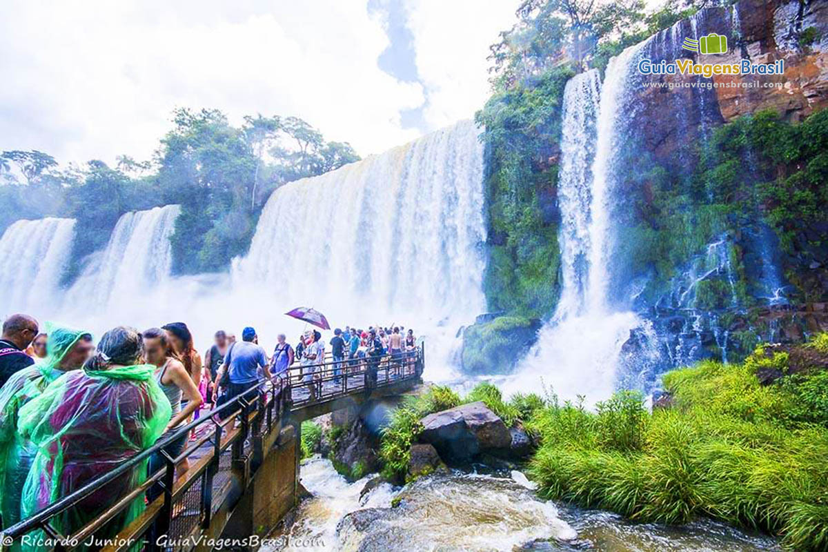 Imagem de turistas encantados com a paisagem e se protegendo das águas.