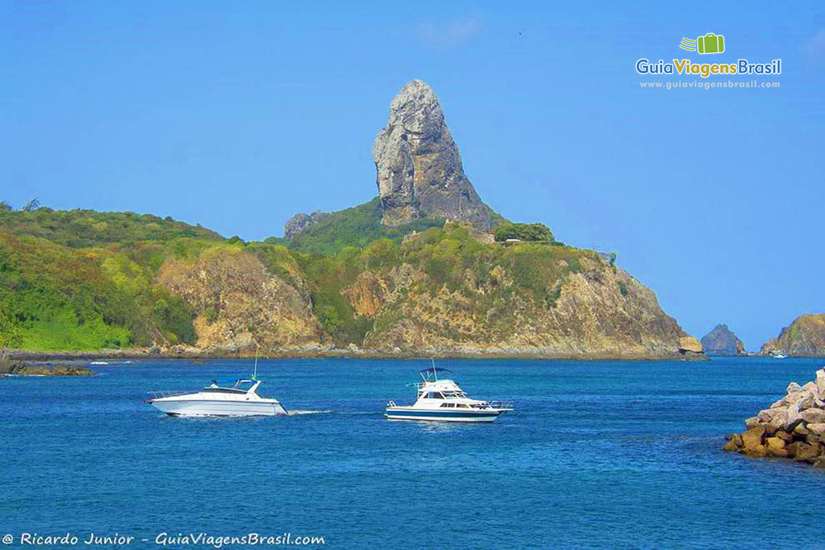 Imagem de uma lancha e um barco parado nas águas azuis do mar, em Fernando de Noronha, Pernambuco, Brasil.