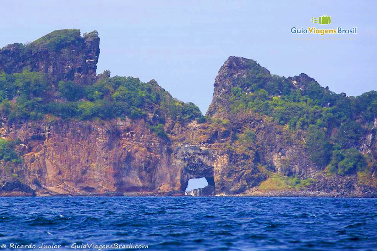 Imagem de uma rocha no alto mar com uma passagem no meio, em Fernando de Noronha, Pernambuco, Brasil.
