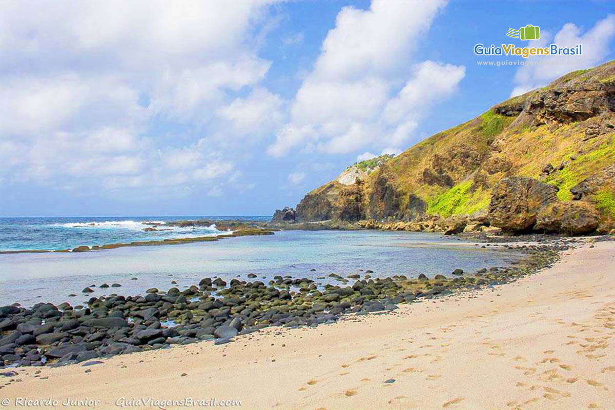 Image da outra extremidade da praia, que tem areia, uma pedras, a piscina natural e ao fundo o mar maravilhoso da Praia da Atalaia, em  Fernando de Noronha, Pernambuco, Brasil. 