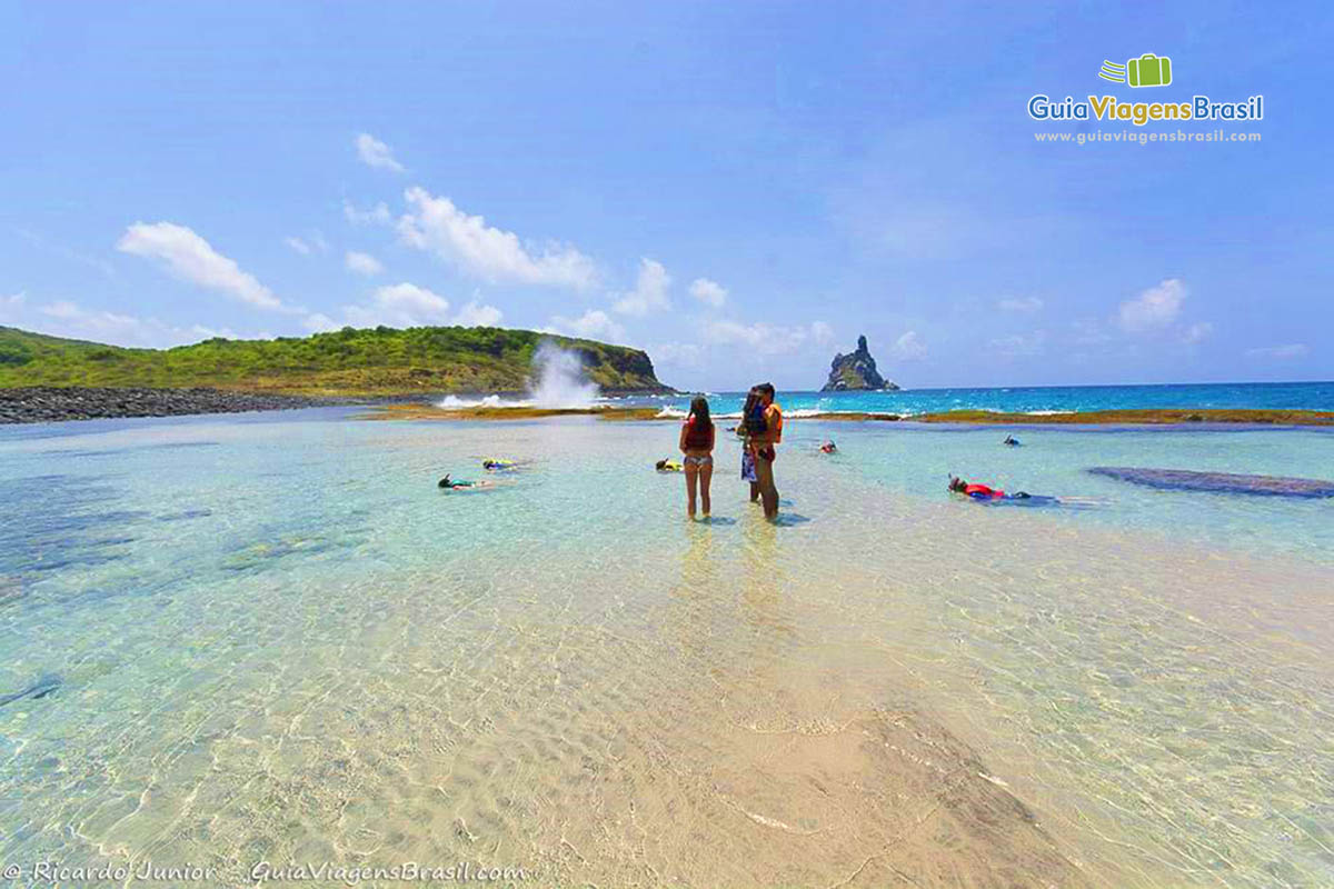 Imagem de alguns turistas em pé na piscina natural e outros aproveitando cada minuto para mergulhar, na Praia da Atalaia, em Fernando de Noronha, Pernambuco, Brasil.