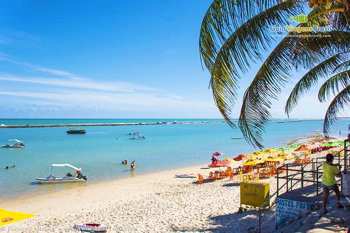 Imagem da ponta da praia, com cadeiras e guarda sol e ao fundo o maravilhoso mar com barcos, em Alagoas, Brasil.