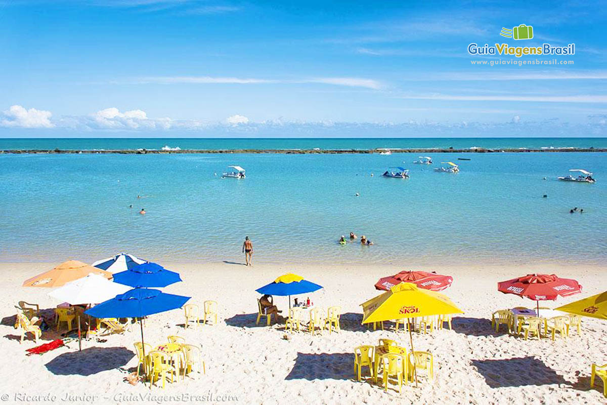 Imagem de guarda sol coloridos espalhados pela areia da praia.