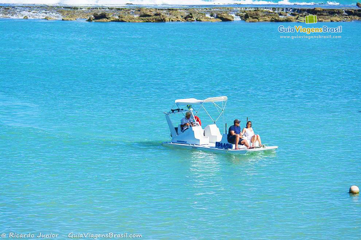 Imagem de barquinho com turistas passeando nas águas claras de Barra de São Miguel, em Alagoas, Brasil.