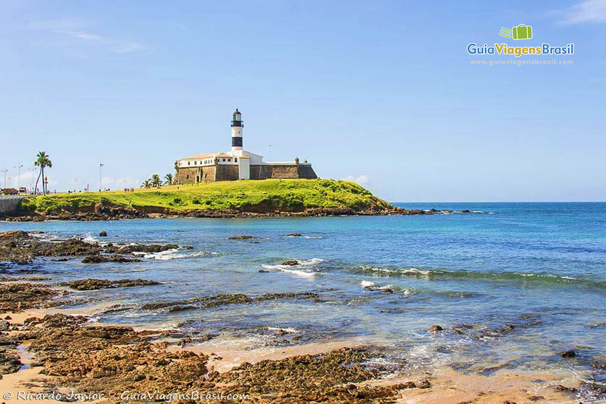 Imagem da praia e ao fundo o farol da Barra.