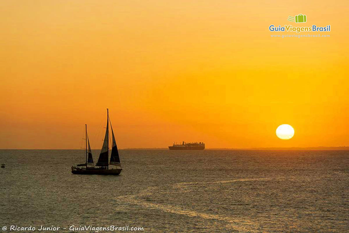 Imagem do sol alaranjado e um barco a vela no mar, uma luz maravilhosa.