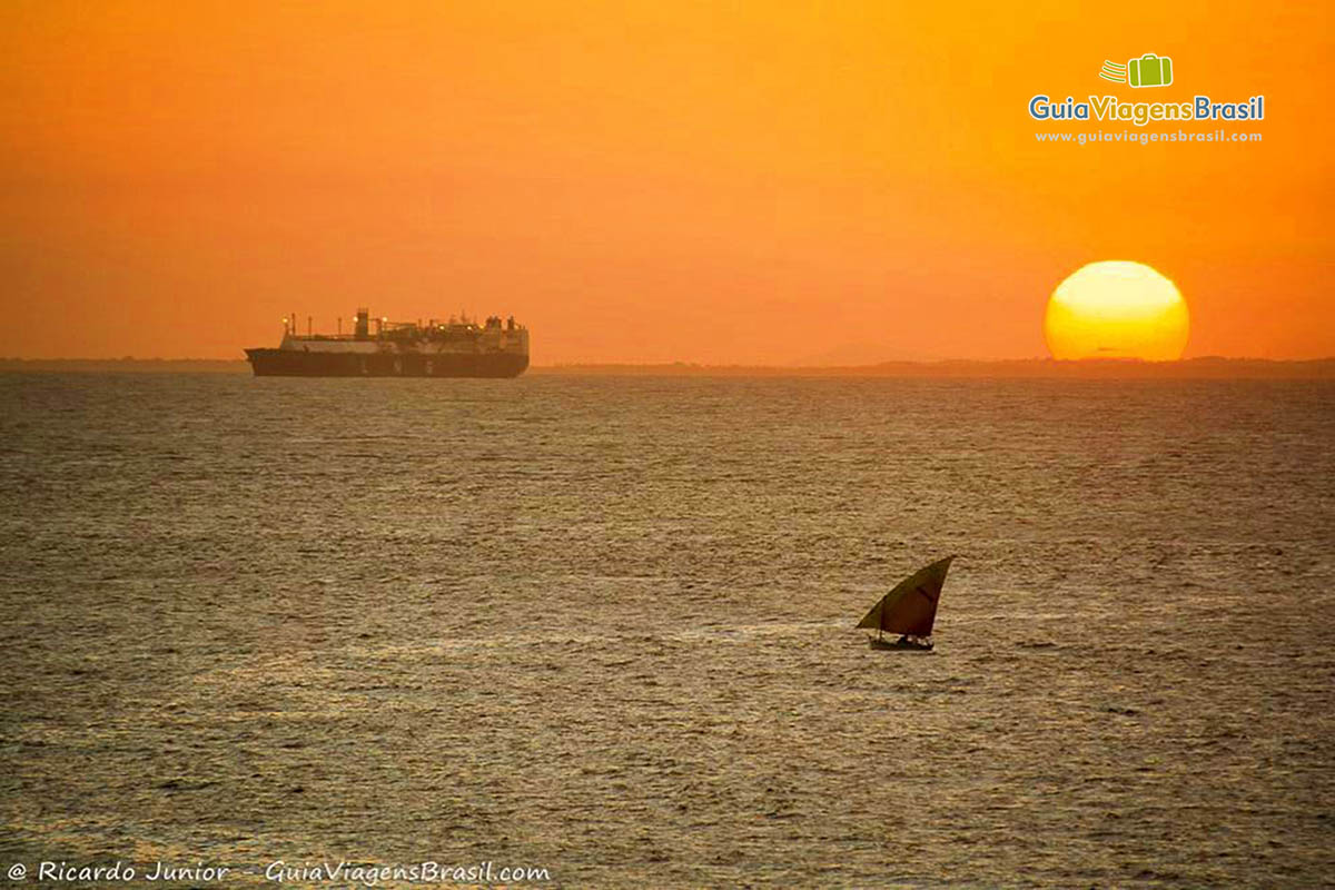 Imagem de barcos no mar da Praia da Barra e sol alaranjado de um fim de tarde.