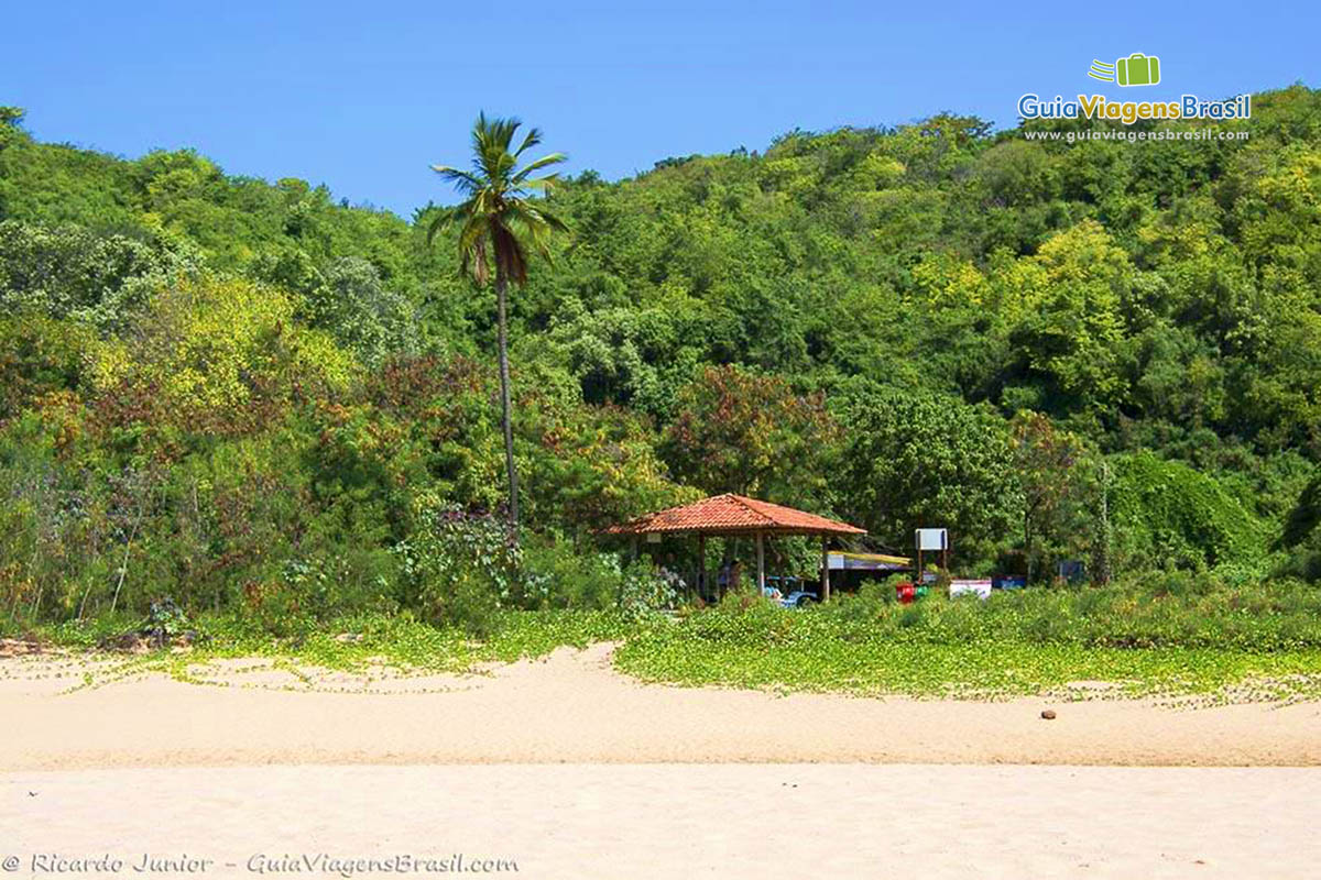Imagem de um quiosque e um Morro atrás com uma vegetação bem verde, na Praia da Cacimba do Padre, em Fernando de Noronha, Pernambuco, Brasil.