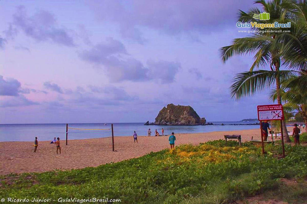 Imagem de pessoas jogando uma partida de volei, enquanto a natureza faz seu show no entardecer, na Praia da Conceição, em Fernando de Noronha, Pernambuco, Brasil.