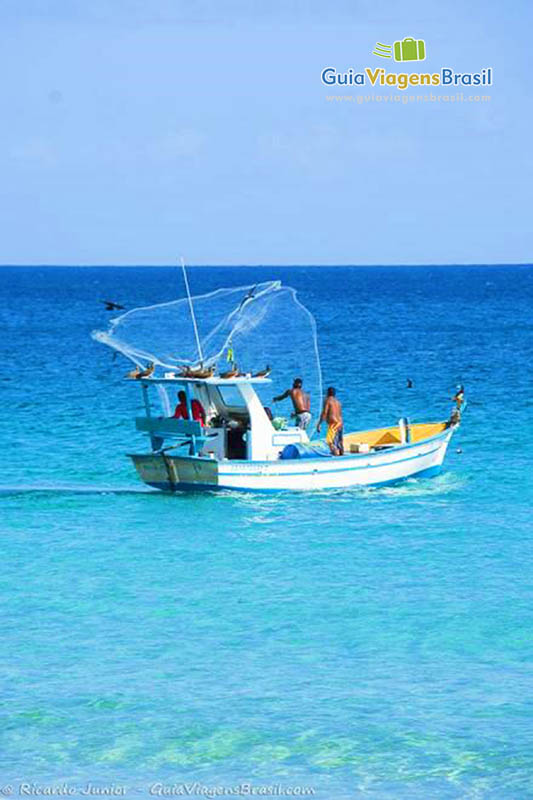 Imagem de pescadores no barco, jogando rede para pescar, na Praia da Conceição, em Fernando de Noronha, Pernambuco, Brasil.