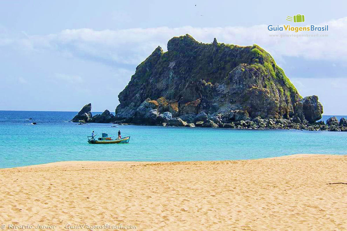 Imagem da praia com areias, barcos de pescador nas águas azuis, da Praia da Conceição, em Fernando de Noronha, Pernambuco, Brasil.