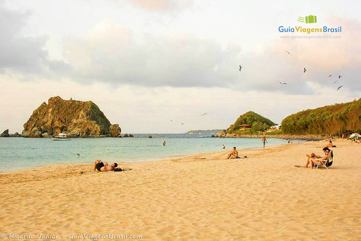 Imagem do canto na praia com pessoas na areia, gaviotas no céu, um cenário maravilhoso, na Praia da Conceição, em Fernando de Noronha, Pernambuco, Brasil.