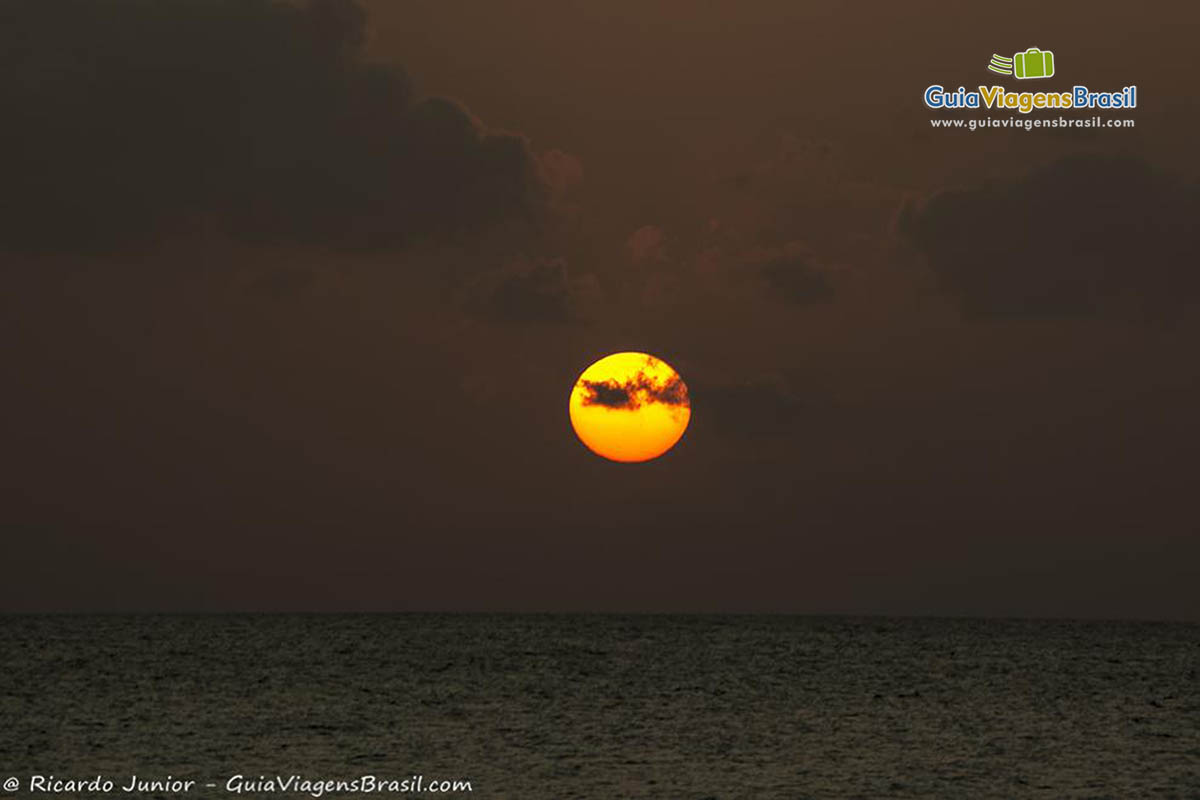 Imagem do sol alaranjado no início da noite na Praia da Conceição, em Fernando de Noronha, Pernambuco, Brasil.