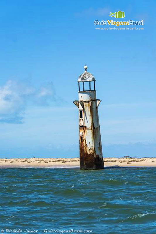 Imagem com vista do mar para a areia da Praia Foz Rio São Francisco e no meio o Farol da praia, em Alagoas, Brasil.