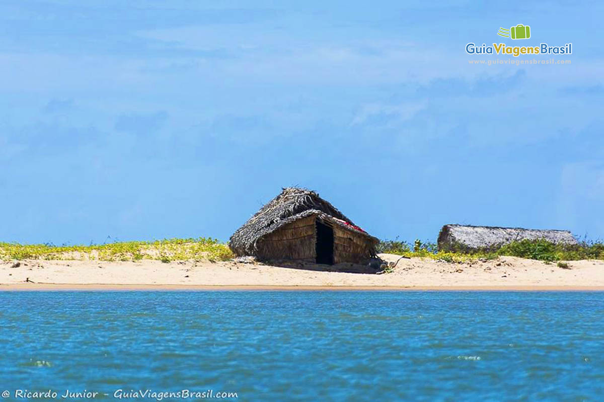 Imagem do mar e ao fundo, nas areias claras, possui cabanas de pescador, em Alagoas, Brasil.