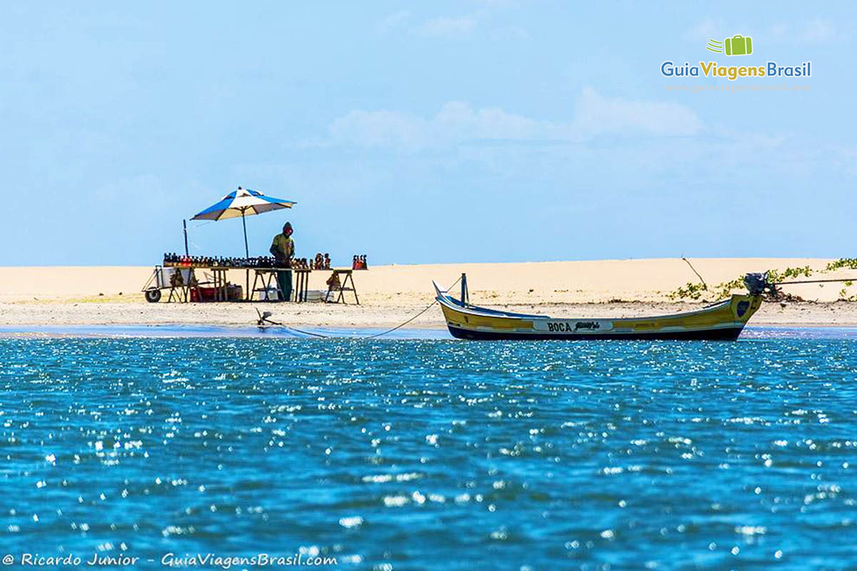 Imagem de um barco de pescador parado e na areia uma barraquinha com vendedor, Foz Rio São Francisco, em Alagoas, Brasil.