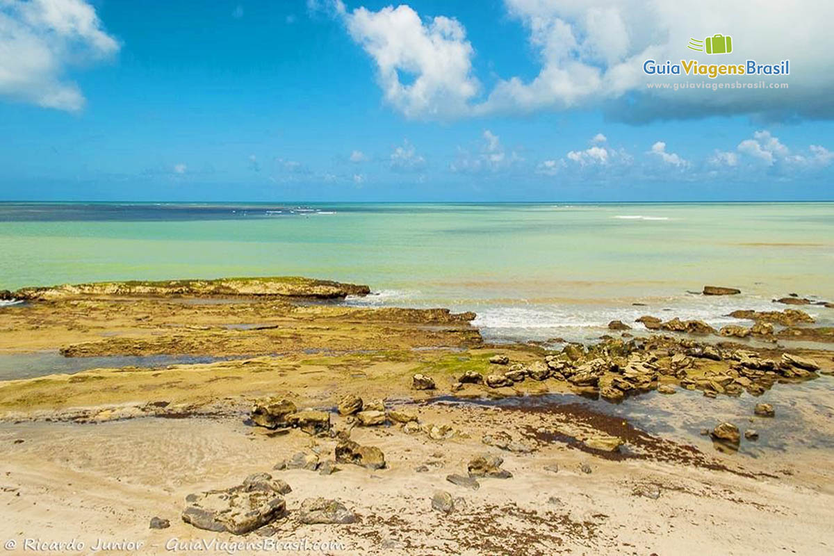 Imagem das pedras e do mar esverdeado e azul da Praia de Bitingui.