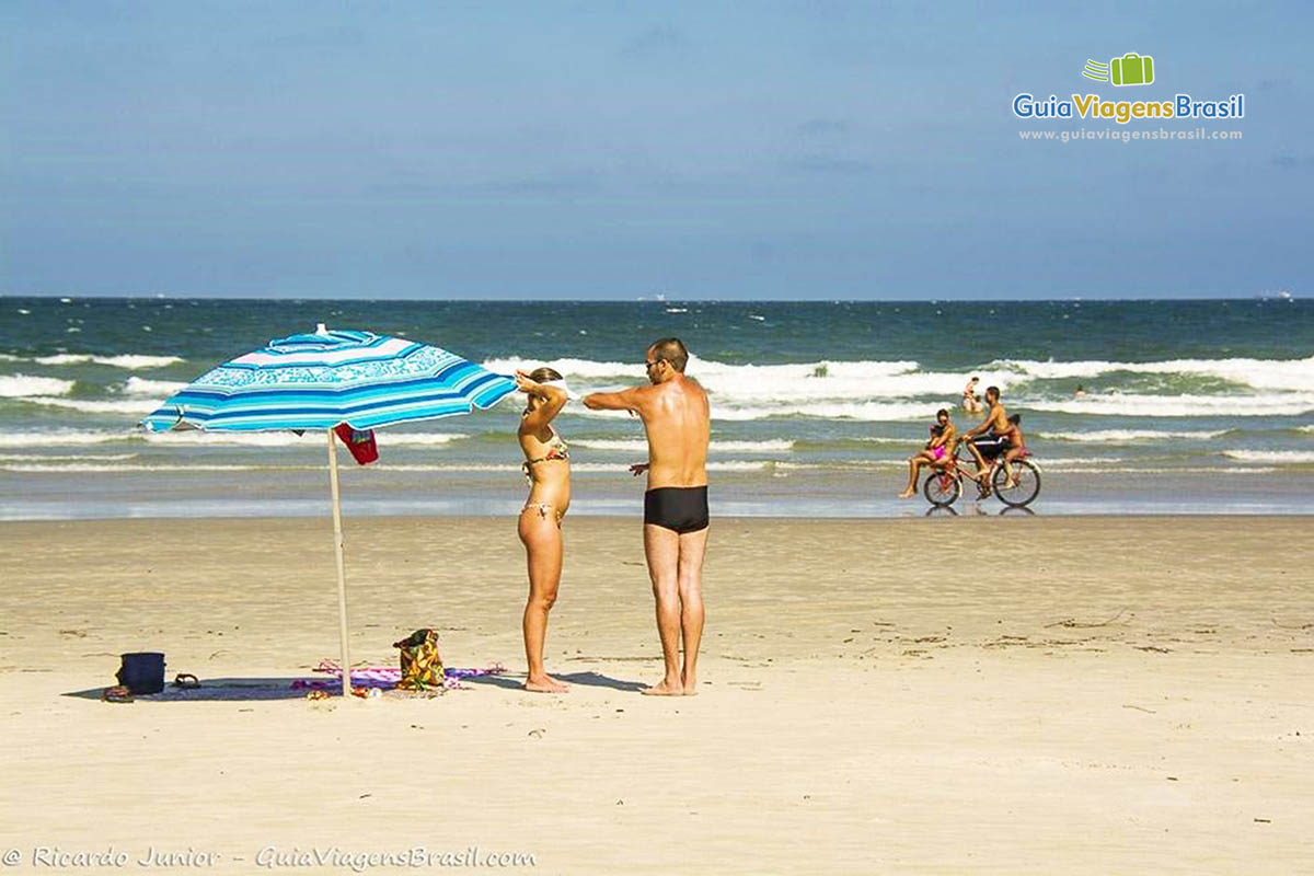 Imagem de casal em pé ao lado do guarda-sol conversando na Praia de Fora, na Ilha do Mel, Paraná, Brasil.