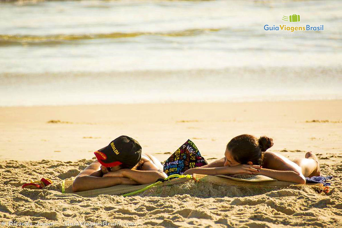 Imagem de duas pessoas tomando sol na Praia de Itapema do Norte, em Itapoá, Santa Catarina, Brasil.