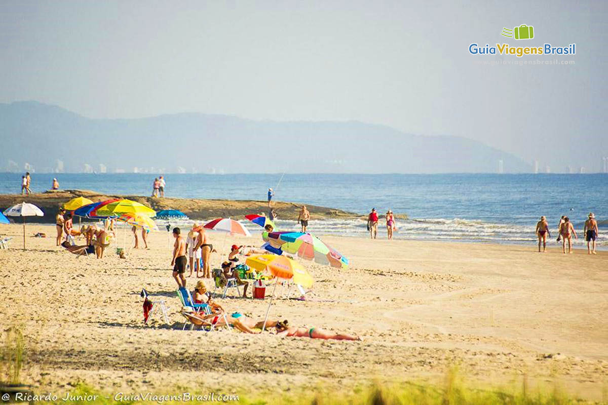 Imagem de turistas na areia com seus guarda sol aproveitando a tarde na Praia de Itapema do Norte, em Itapoá, Santa Catarina, Brasil.