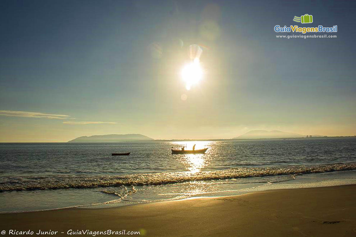 Imagem da luz do sol refletindo nas águas do mar e um barco de pescador parado nas águas, na Praia de Itapoá, em Itapoá, Santa Catarina, Brasil.