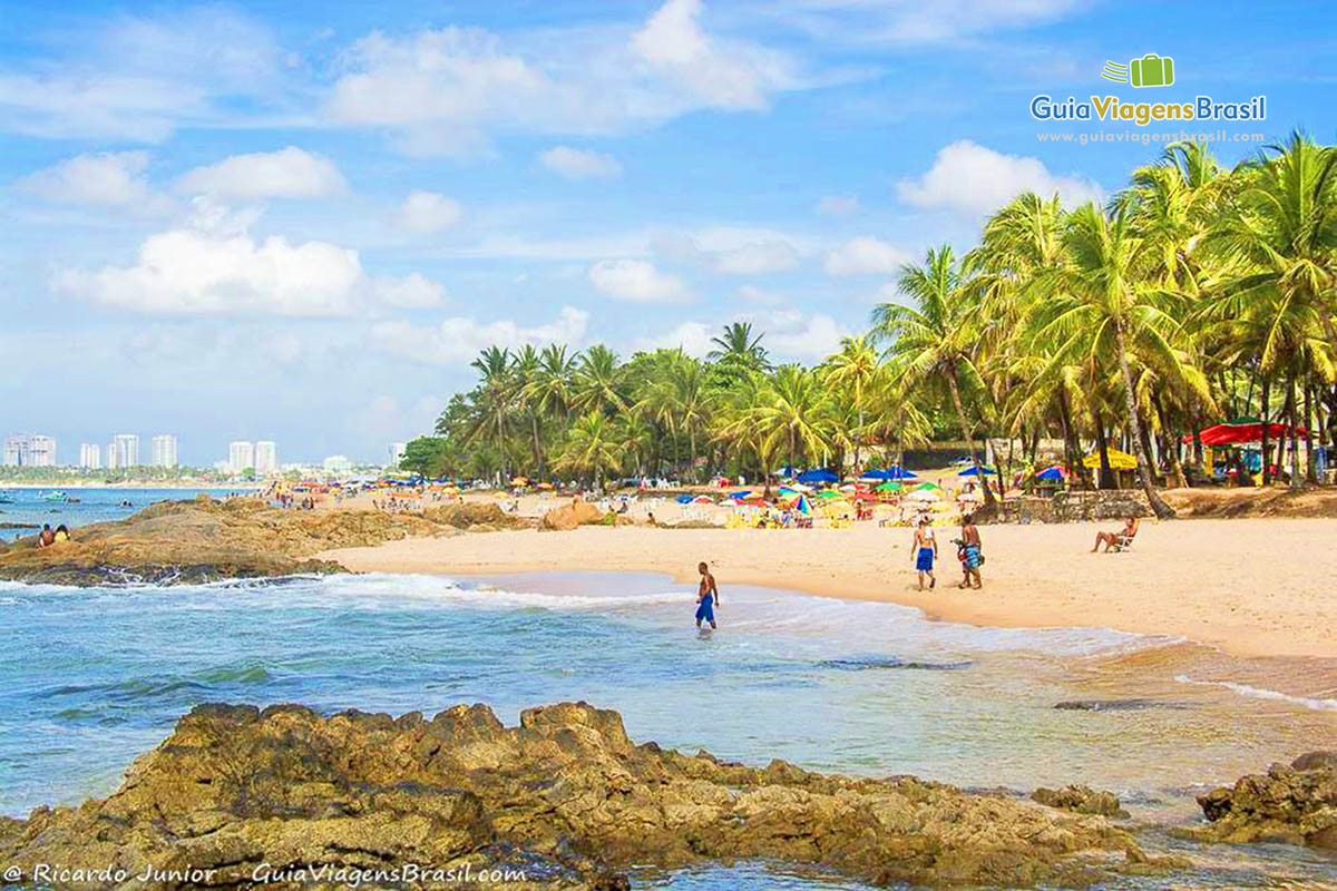 Imagem de turistas nas águas claras da Praia de Itapuã.