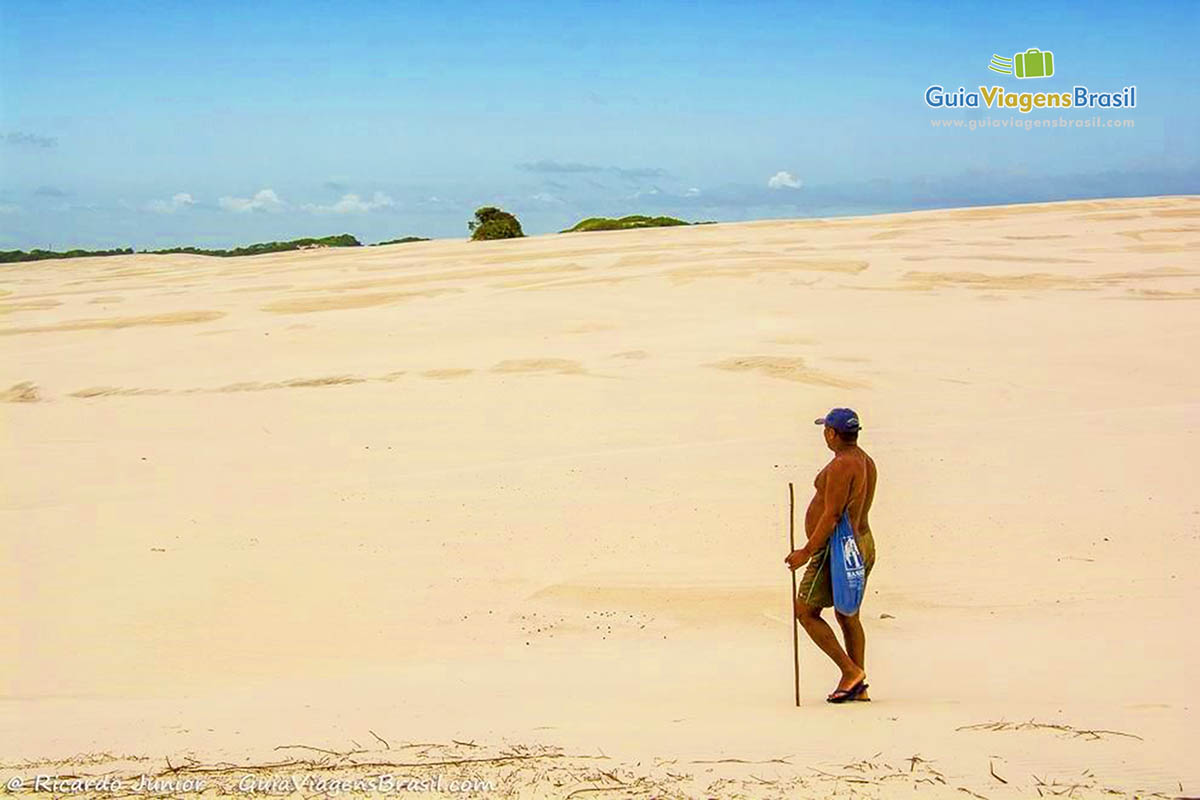 Imagem de um senhor caminhando nas dunas e admirando a paisagem.
