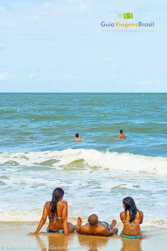 Imagem de três pessoas sentados na beira do mar, se deliciando com as águas da Praia de Mundaí.