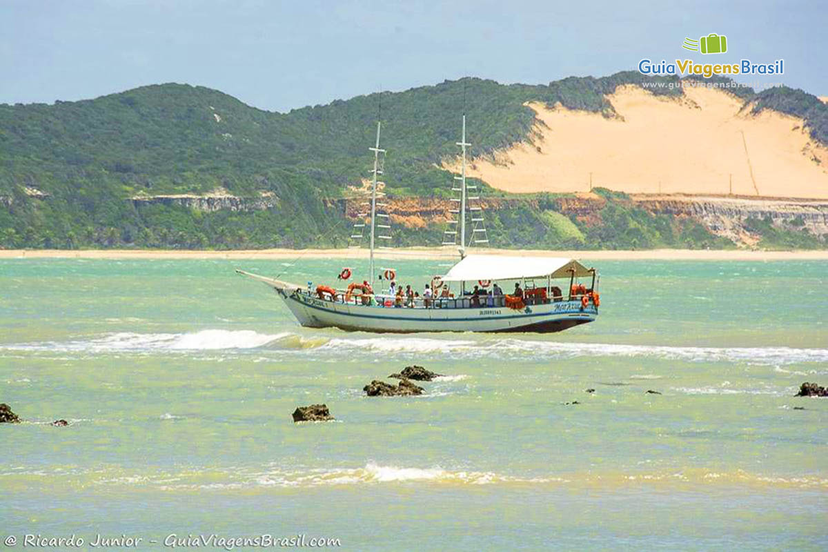 Imagem de barco de passeio entre as pequenas pedras da Praia de Pipa.