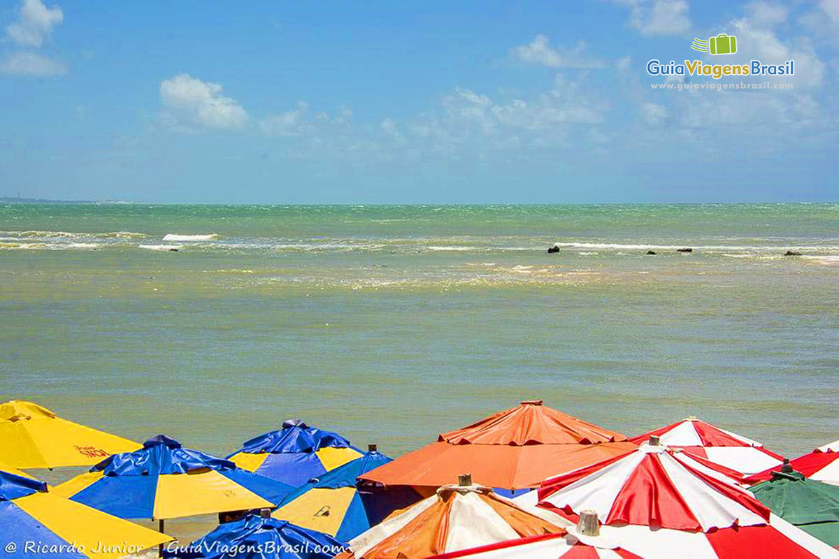 Imagem do topo de guarda sol coloridos e ao fundo a Praia de Pipa.