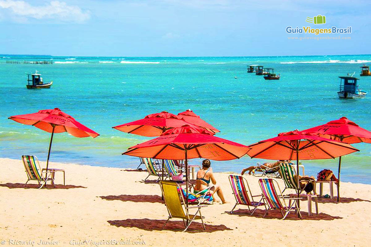 Imagem de guarda sol vermelho organizados na areia e ao fundo a excelente Praia de Ponta Verde, em Maceió, Alagoas, Brasil.