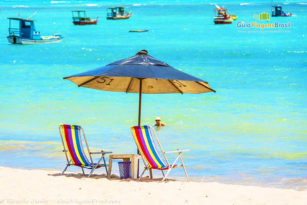 Imagem guarda sol e duas cadeiras a espera de turista e ao fundo bela vista da piscina natural da Praia de Ponta Verde, em Maceió, Alagoas. 