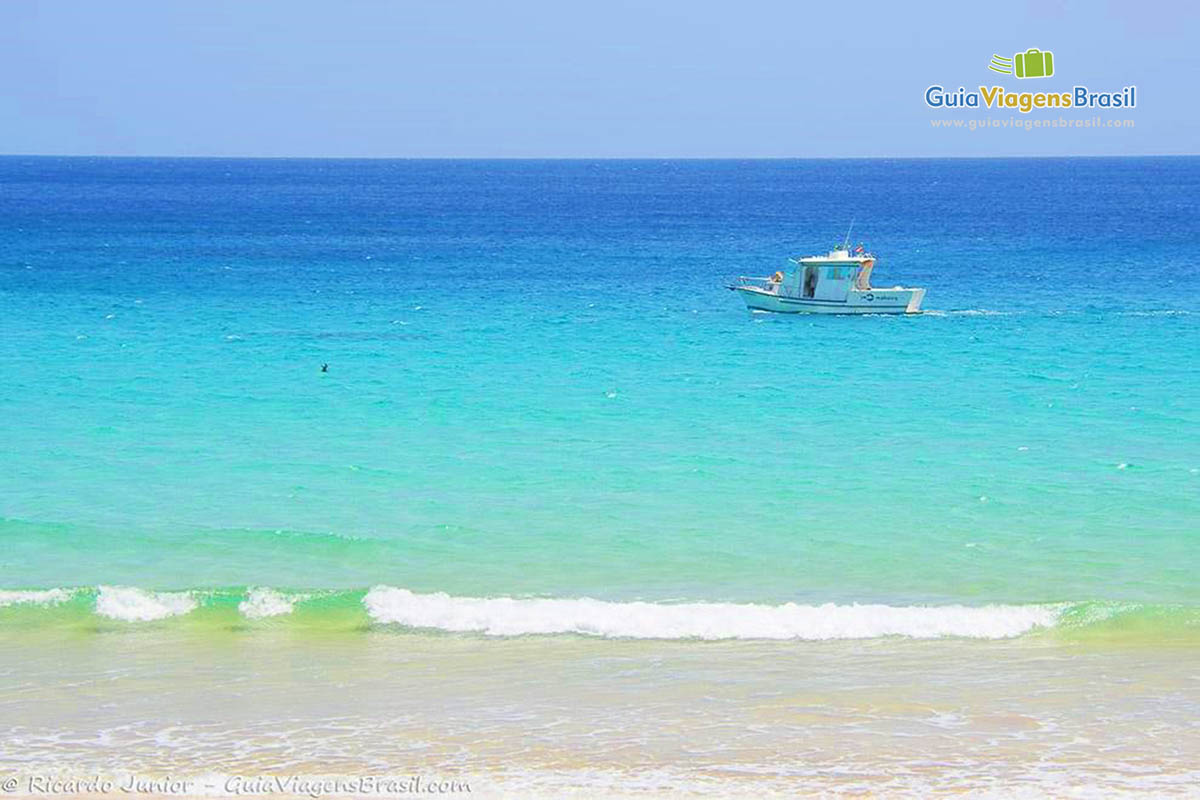 Imagem de barco nas águas transparentes da Praia da Quixabinha, em Fernando de Noronha, Pernambuco, Brasil.