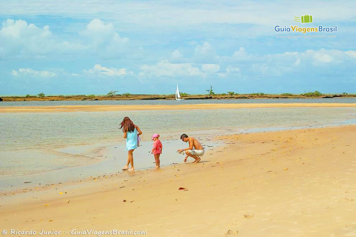 Imagem de crianças com o pai procurando conchinhas na praia de Santo André.