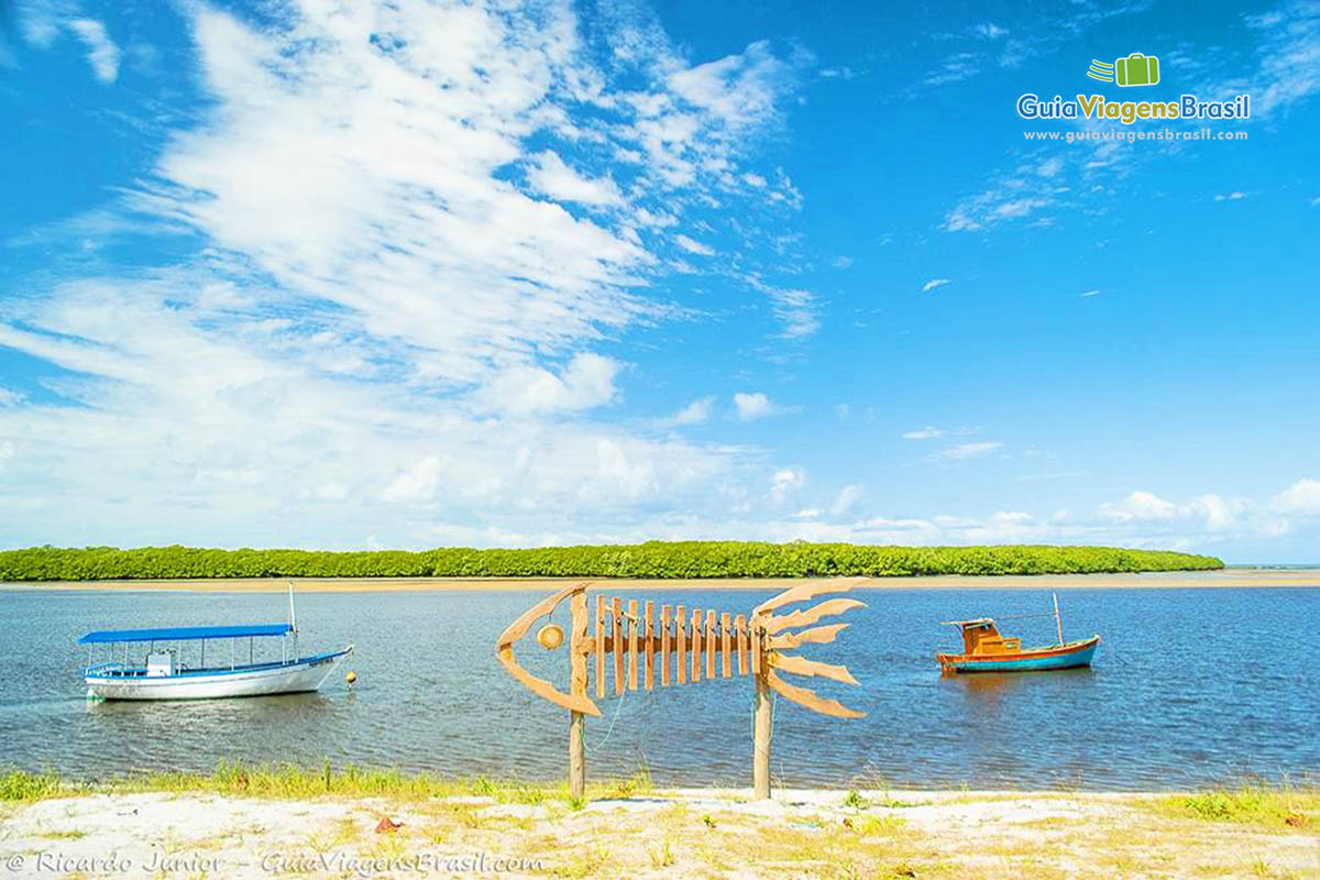 Imagem de dois barco de pescadores no mar e na areia no meio dos barcos um peixe feito de madeira na Praia de Santo André.