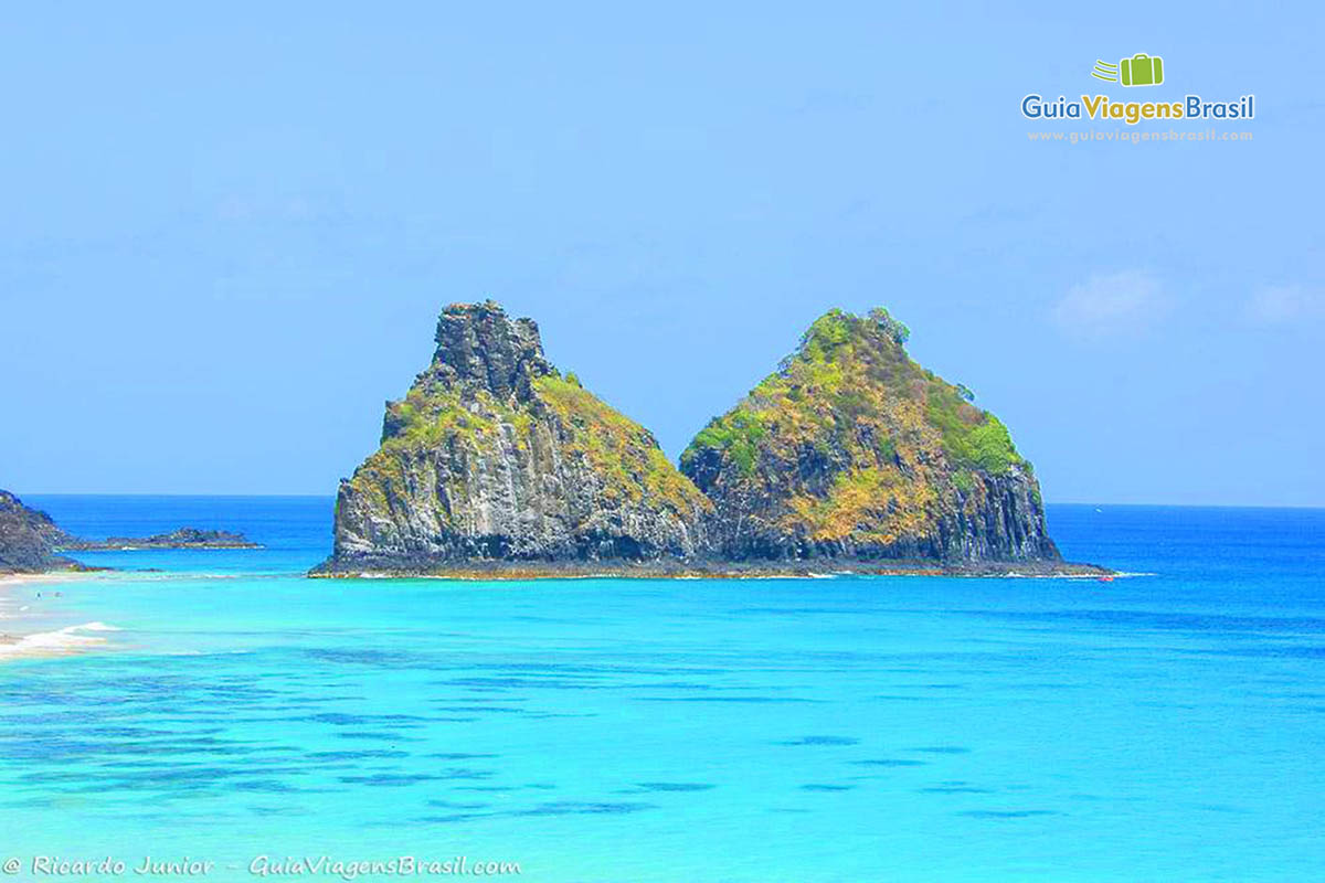 Imagem mais aproximada do Morro Dois Irmãos em volto por águas azuis da Praia do Bode, em Fernando de Noronha, Pernambuco, Brasil.