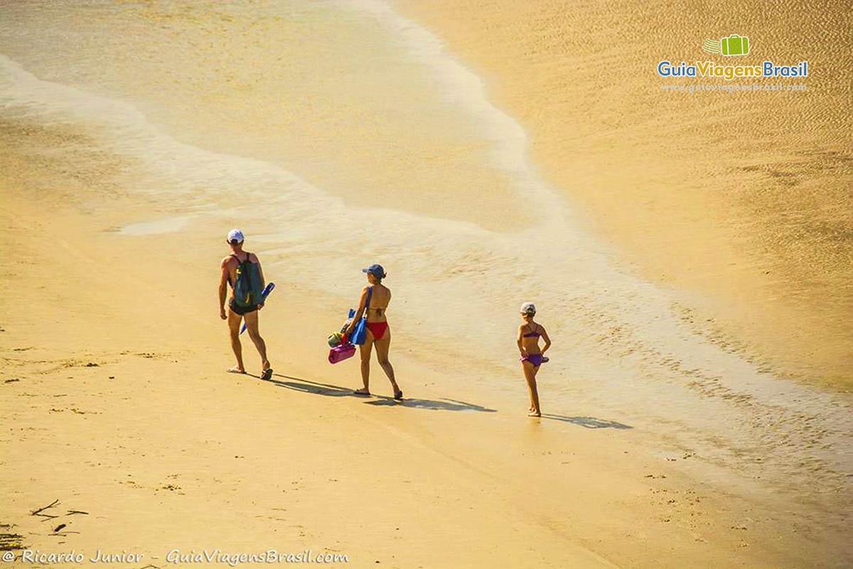 Imagem de três turistas chegando e andando nas areias da Praia do Farol, na Ilha do Mel, Paraná, Brasil.